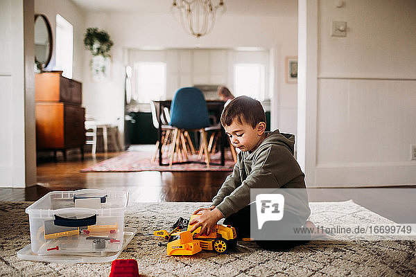 Kleiner Junge sitzt drinnen und baut einen Spielzeugtraktor zusammen