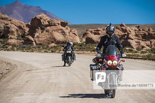 Zwei Freunde fahren auf einem Tourenmotorrad auf einer staubigen Straße in Bolivien