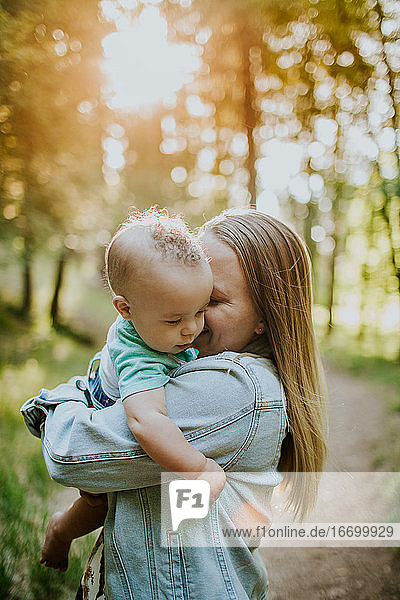 Vertical of happy mother snuggling baby boy outside in forest
