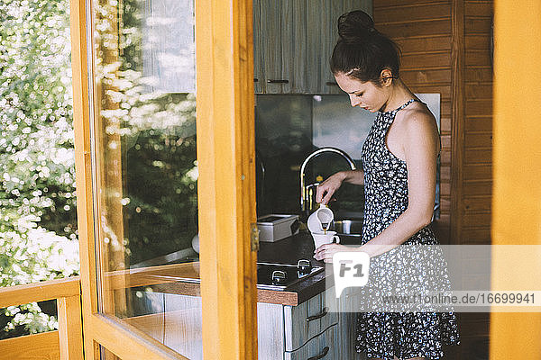 Junge Frau im Sommerkleid schenkt in der Küche Kaffee ein