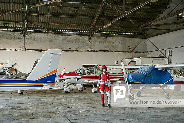 Junge Fallschirmspringerin in einem Flugzeughangar  umgeben von Flugzeugen
