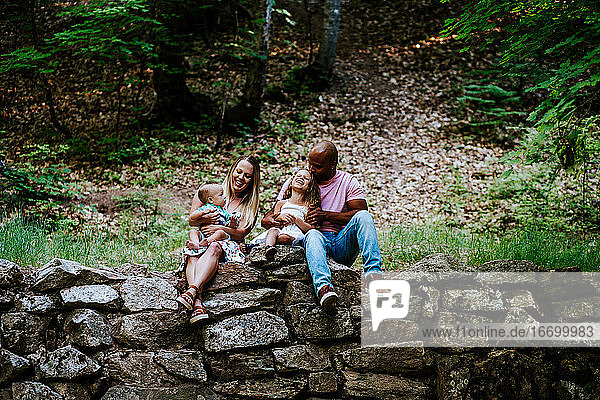 Happy multiracial family laughing while sitting on rocks in forest