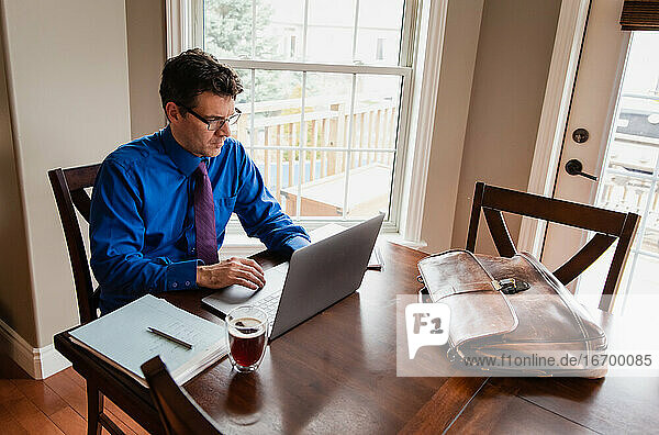 Mann in Hemd und Krawatte arbeitet von zu Hause aus am Computer am Esstisch.