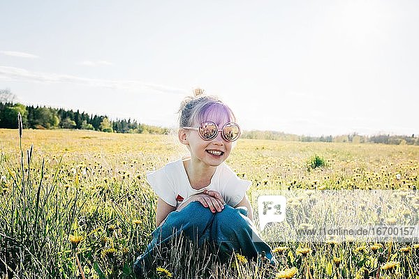 junges Mädchen saß mit Sonnenbrille auf einem Blumenfeld im Sommer