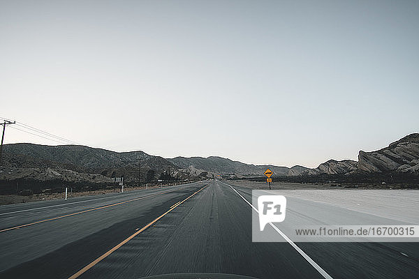 Leerer Highway in Kalifornien kurz nach Sonnenuntergang mit gelbem Straßenschild und Bergen in der Ferne während der Coronavirus-Pandemie