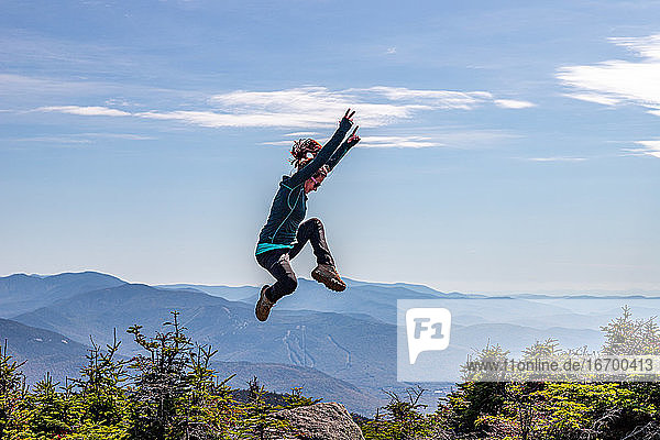 Junge sportliche Frau  die auf einem Berggipfel in Pose springt.