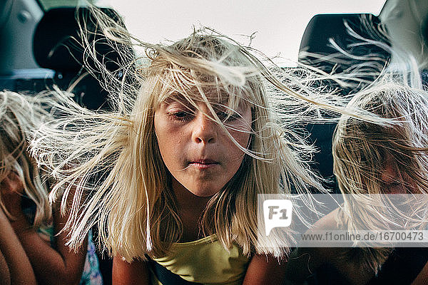 Jungen und Mädchen auf dem Rücksitz eines Autos mit im Wind wehenden Haaren