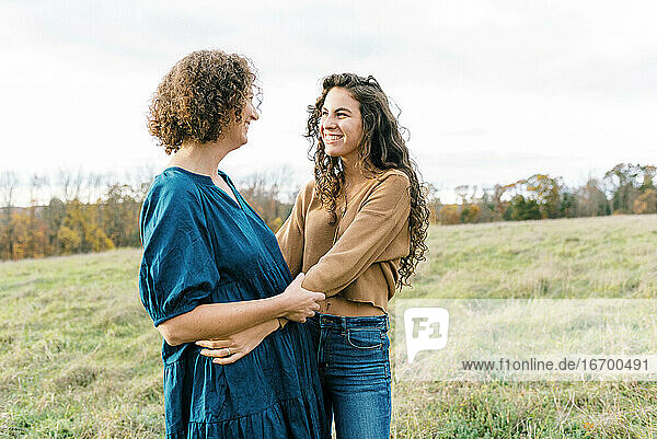 A happy mother and her teenage daughter standing together in a field