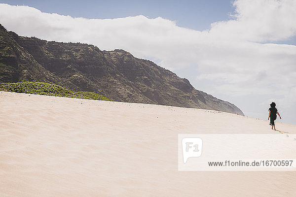 Frau geht einen sandigen Hügel hinauf in Richtung Berge auf Hawaii