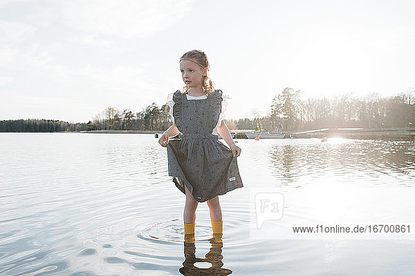 ein junges Mädchen stand bei Sonnenuntergang in einem Kleid im Wasser