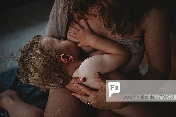 Boy breastfeeding naked with his hand on mom's breast showing skin