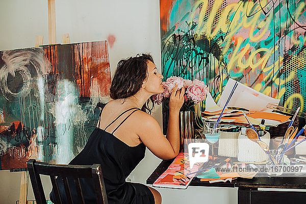 Künstlerin riecht an Blumen  während sie in ihrem Atelier sitzt