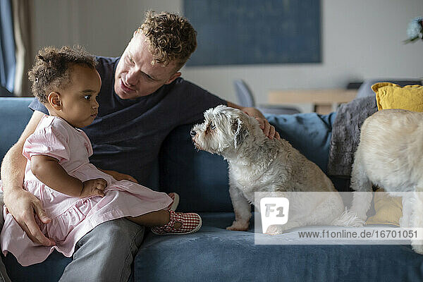 A caucasian father sits with his biracial daughter and puppy