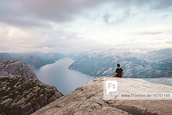 Mann sitzt in einem Felsen am Rande einer Klippe am Preikestolen  Norwegen