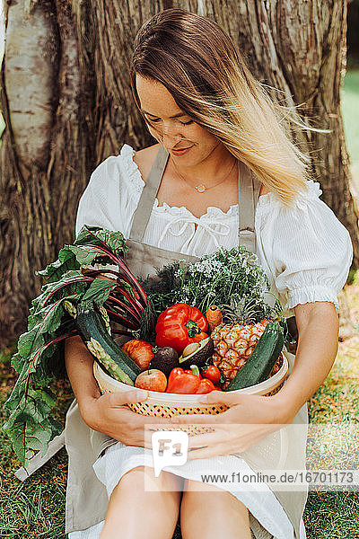 Junge Frau in rustikaler Kleidung hält einen Korb mit Gemüse