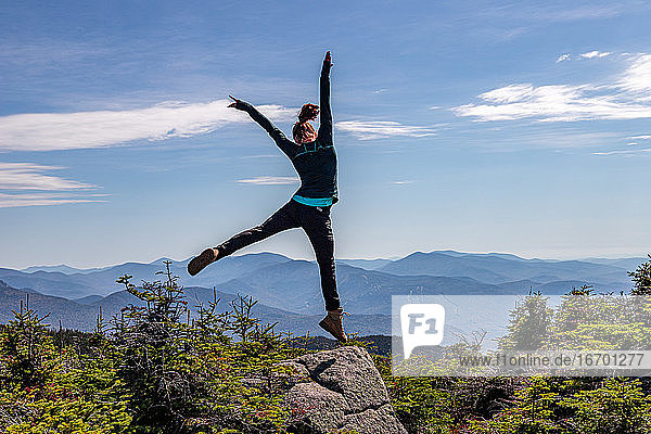 Junge Frau springt auf dem Gipfel eines Berges.