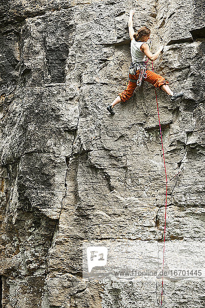 Junge Frau beim Klettern an einer Felswand in Frankreich