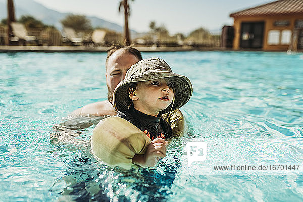 Nahaufnahme eines Kleinkindes und eines Vaters beim Schwimmen im Pool im Urlaub