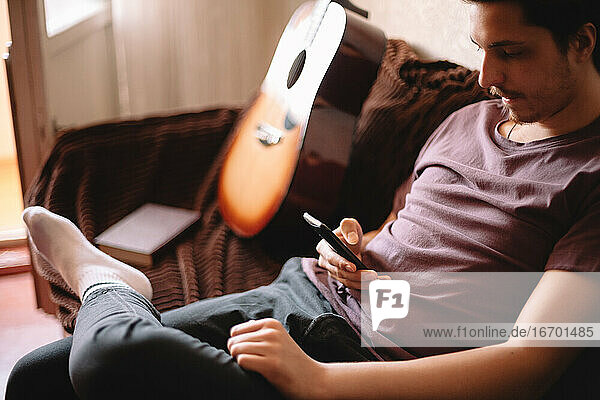 Seriöser junger Mann  der sein Smartphone benutzt  während er zu Hause sitzt