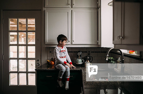 Junge sitzt auf dem Küchentisch und hilft beim Kaffeekochen für das Frühstück