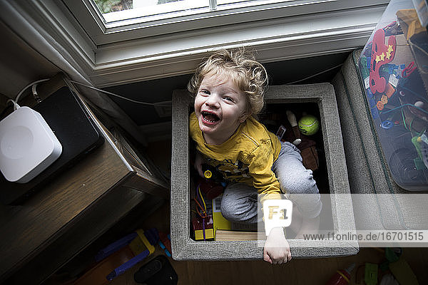Lachender Junge sitzt in der Spielzeugkiste neben den Aufbewahrungsbehältern und blickt in die Kamera