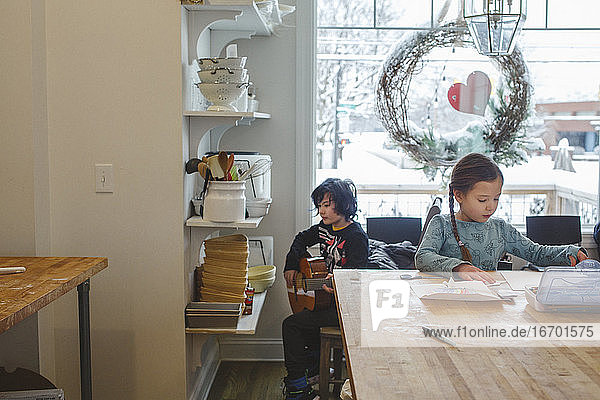 Zwei Kinder sitzen zusammen in der Küche und machen Musik und Kunst am Fenster