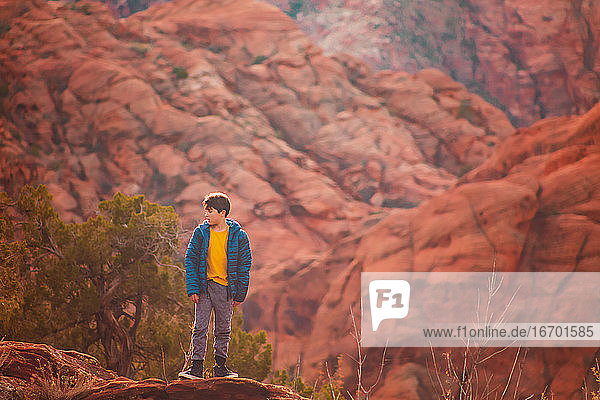 Boy hiking on trail by the red sandstone cliffs and mountains in Utah