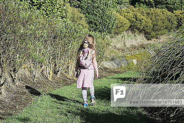 Junges Mädchen spaziert mit ihrer Puppe im Rucksack im Naturschutzgebiet