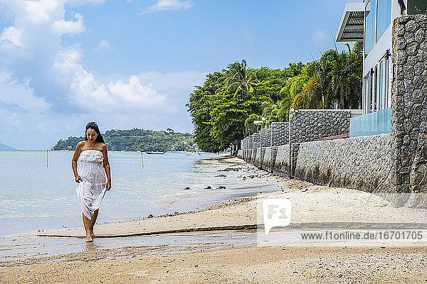 schöne Frau in weißem Kleid  die am Strand von Phuket spazieren geht
