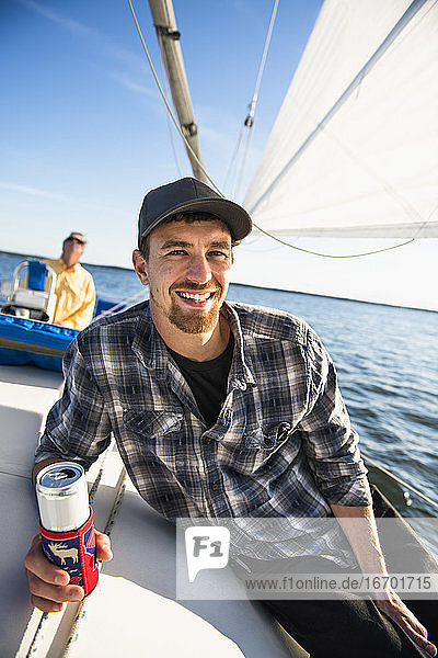 Junger Mann genießt Sommer Segelregatta während der goldenen Stunde mit Getränk