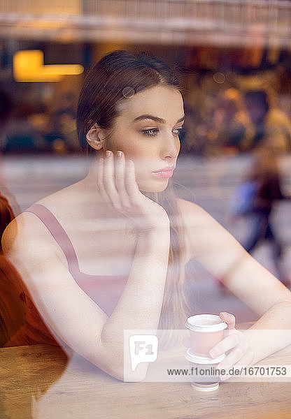 Porträt einer jungen Frau in einem Café  die aus dem Fenster schaut