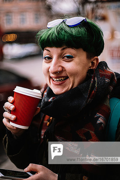 Porträt einer glücklichen nicht-binären Hipster-Frau  die in der Stadt Kaffee trinkt