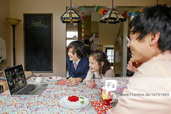 A smiling family sits at table on a zoom meeting birthday party