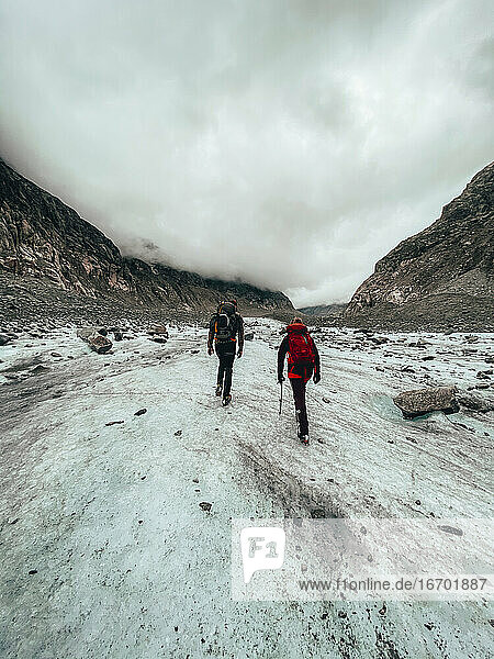 Zwei Bergsteiger wandern auf einem Gletscher unter bewölktem Himmel