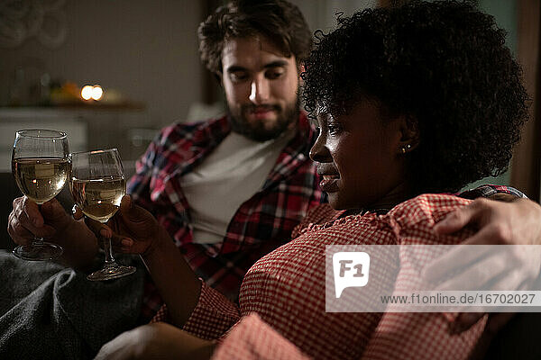 Multiethnisches Paar chillt auf Sofa mit Wein