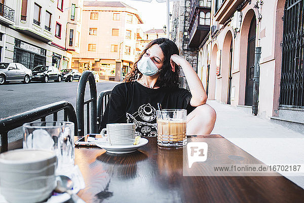 Mädchen trinkt einen Kaffee auf der Terrasse einer Bar mit einer Maske