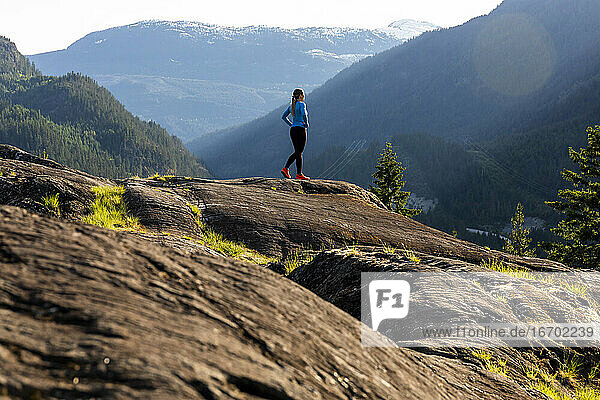 Seitenansicht einer starken Sportlerin  die während eines Fitnesstrainings auf dem Land bei Sonnenuntergang eine Pause vom Laufen macht.