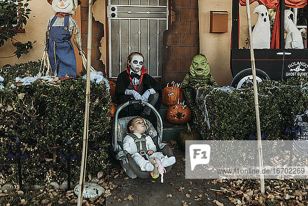 Drei männliche Geschwister in Halloween-Kostümen posieren zu Hause