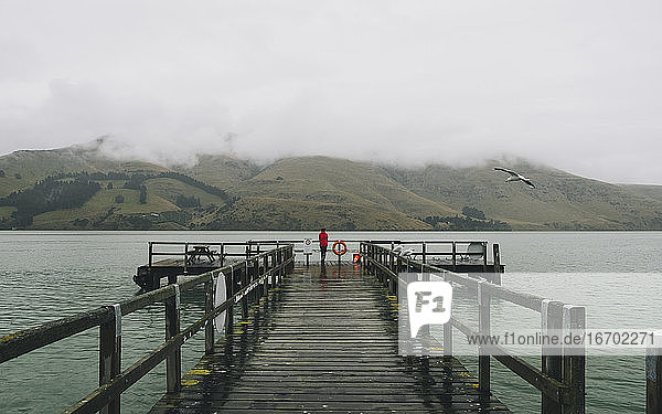Woman on a red jacket standing at Port Levy Jetty  Banks Peninsula  NZ