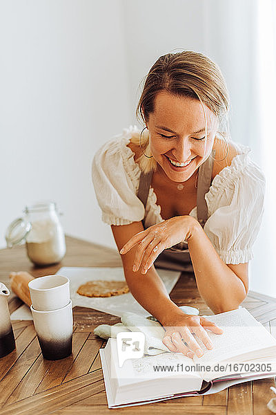 Lächelnde Frau liest ein Rezeptbuch beim Kochen in der Küche