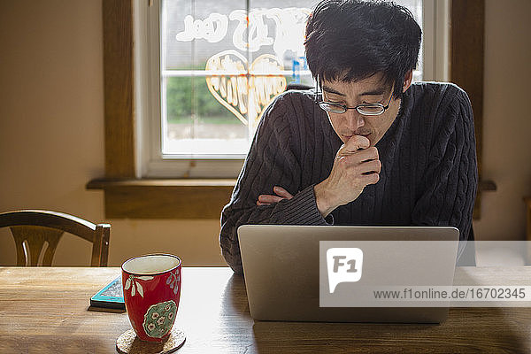 Ein Mann sitzt an einem Esszimmertisch am Computer und arbeitet von zu Hause aus