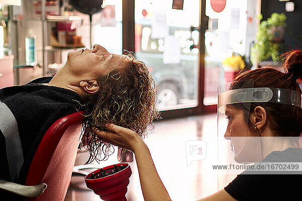 Friseurin mit Gesichtsschutz trocknet die Haare ihrer Kundin in ihrem Salon