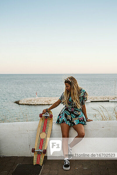 Junge Frau mit langem Brett skaten vor dem Mittelmeer
