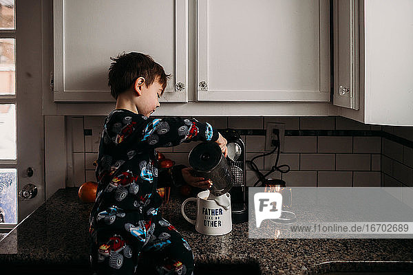 Junge in Küche gießt Milch in Kaffeetasse für Vater