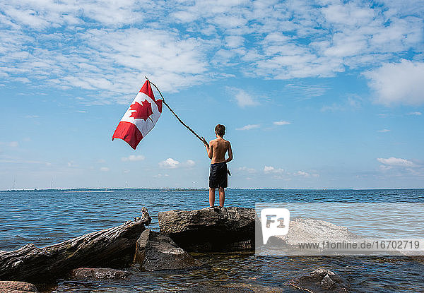Junge hält an einem Sommertag am Ufer eines Sees die kanadische Flagge in die Luft.