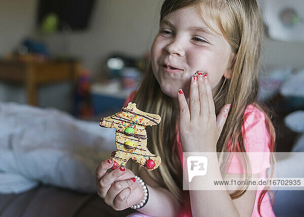 Young girl eating a gingerbread man in her bedroom