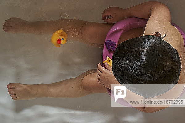 Glückliches Baby spielt mit Seifenschaum im heimischen Badezimmer. Gummi-Ente in Schaumbad.