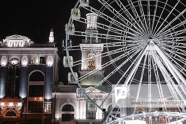 Illuminated Ferris wheel against building in night winter city