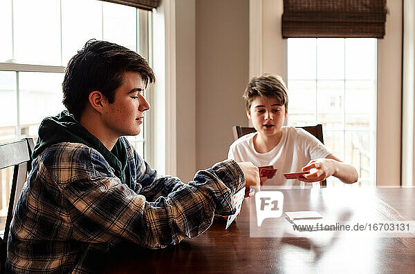 Zwei Teenager spielen zusammen am Küchentisch Karten.