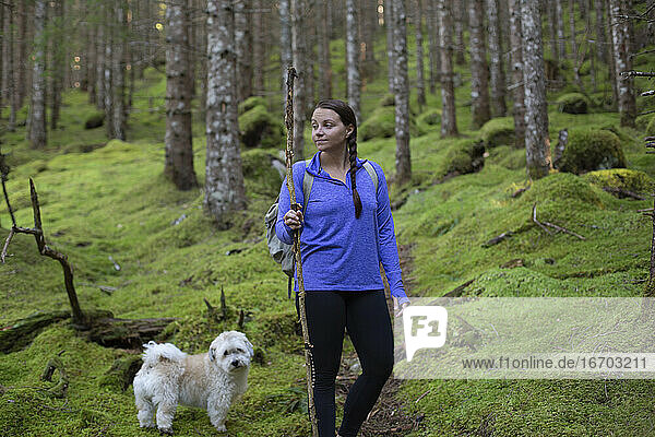 Eine junge Frau mit einem Spazierstock auf einem moosigen Weg mit ihrem Hund